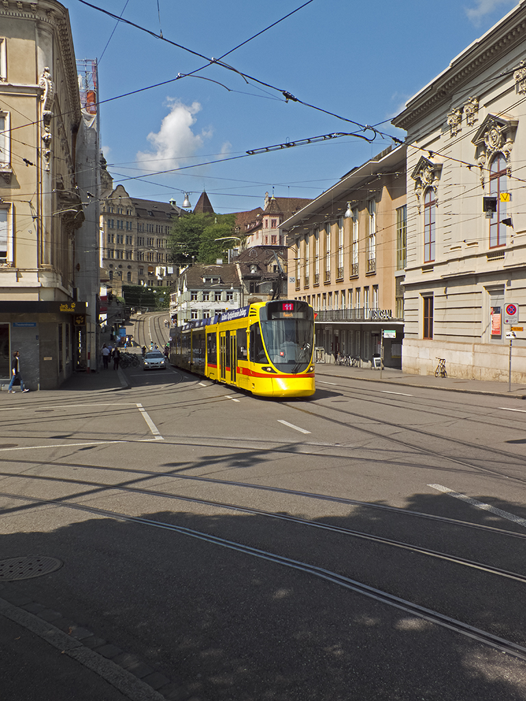 Neben den grünen Trams der Basler Verkehrsbetriebe (BVB) ist auch das gelb der Baselland Transport (BLT) in den Straßen Basels allgegenwärtig. Letzteres Unternehmen setzt seit einigen Jahren Tango-Trams von Stadler ein, von denen eines hier auf der Linie 11 nach Aesch den Steinenberg zwischen Barfüsserplatz und Bankverein erklimmt.